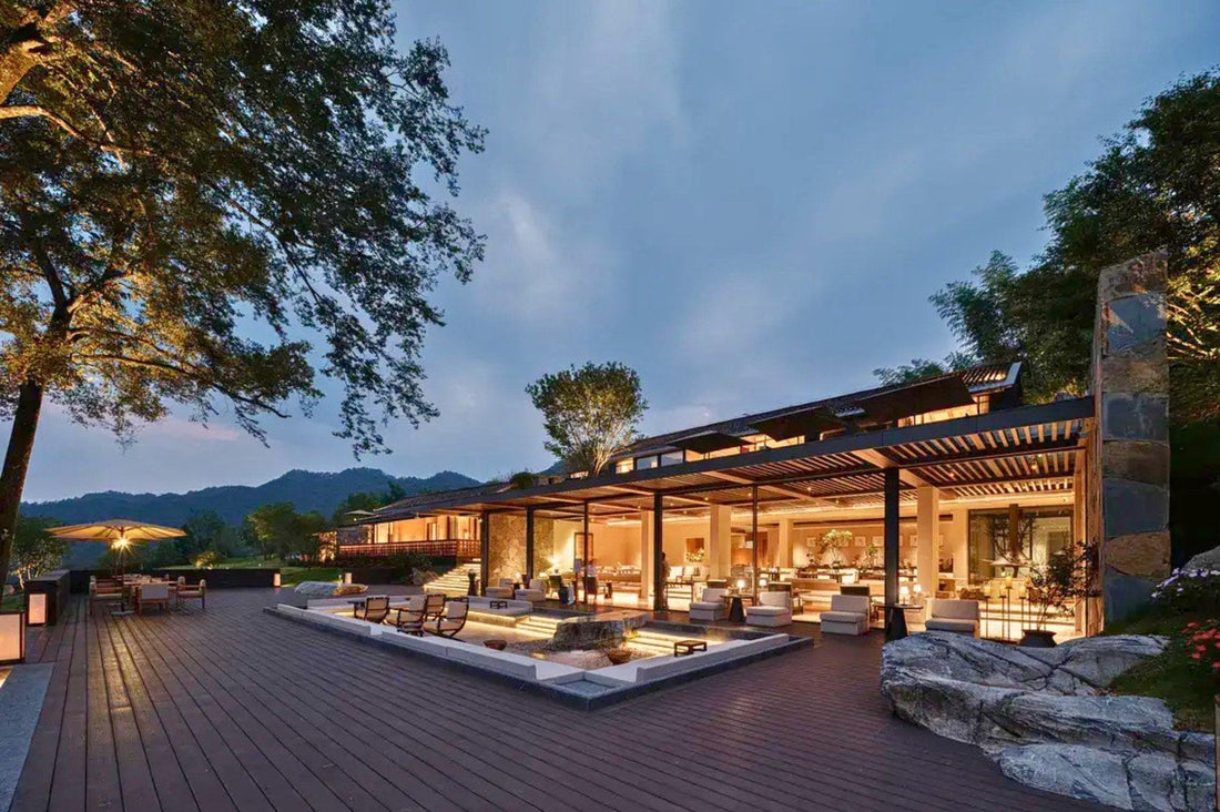 Twilight view of the hotel's open-air terrace with illuminated wooden deck, stone water feature and mountain backdrop